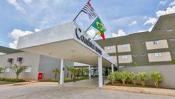 Entrada de un hotel con un letrero que dice "Confort Inn" y dos banderas, una brasileña y otra del Reino Unido.
