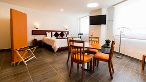 A hotel room with a bed, a desk, chairs, a TV, and a large window. - Hotel Misión Puebla Angelopolis (Puebla)