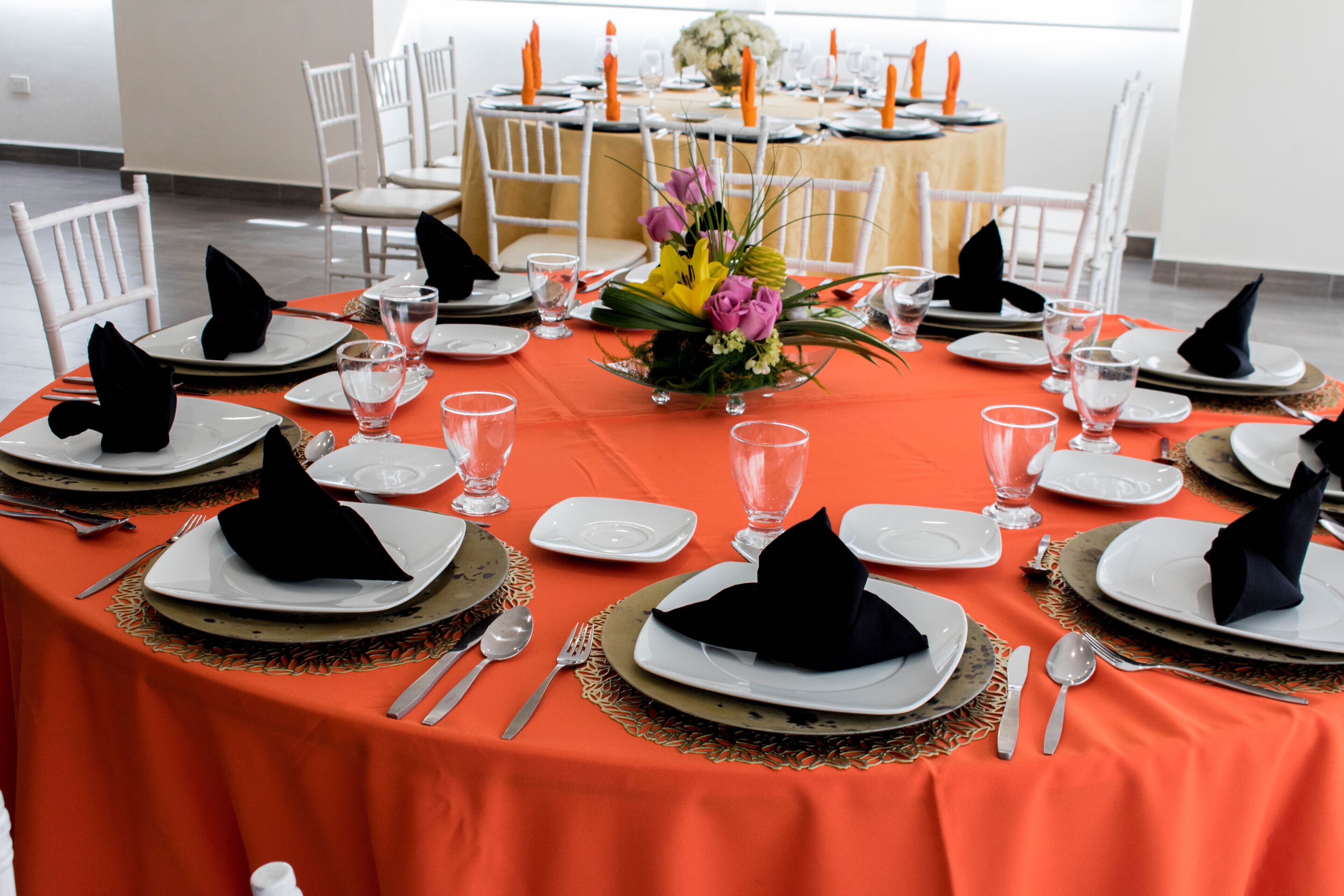 A round table set for a formal dinner with white plates, black napkins, and a centerpiece of flowers.