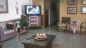 A reception area with a television, seating, a potted plant, and framed pictures on the wall. - Hotel Graúnas (São Carlos)