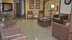 A lobby with wicker furniture, a television, framed artwork, and a clock on the wall. - Hotel Graúnas (São Carlos)