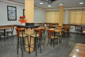 A dining area with multiple tables and chairs, a central bar area, and a ceiling fan. - Hotel Graúnas (São Carlos)
