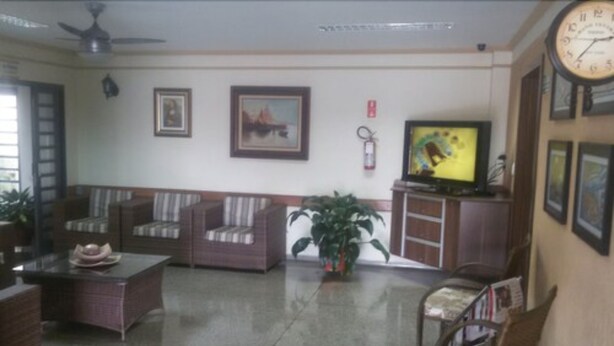 A living room with a sofa, chairs, a television, a clock, and a plant. - Hotel Graúnas (São Carlos)