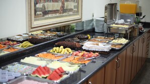 A buffet with various food items including fruits, pastries, and a juice dispenser. - Hotel Graúnas (São Carlos)