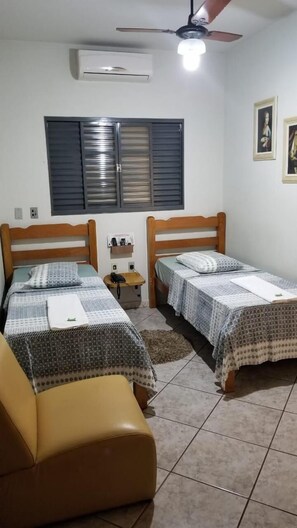 A room with two beds, a ceiling fan, an air conditioning unit, a window with blinds, and a small rug. - Hotel Graúnas (São Carlos)