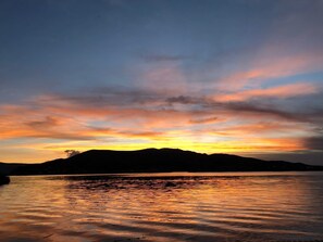 Un atardecer sobre una superficie acuática tranquila con siluetas de montañas al fondo.