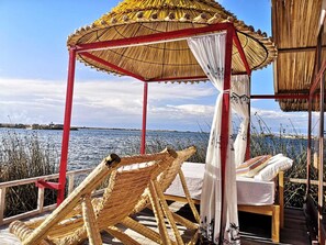 Un kiosque à toit de chaume, doté d’une toiture blanche et d’une structure rouge, surplombant une étendue d’eau.