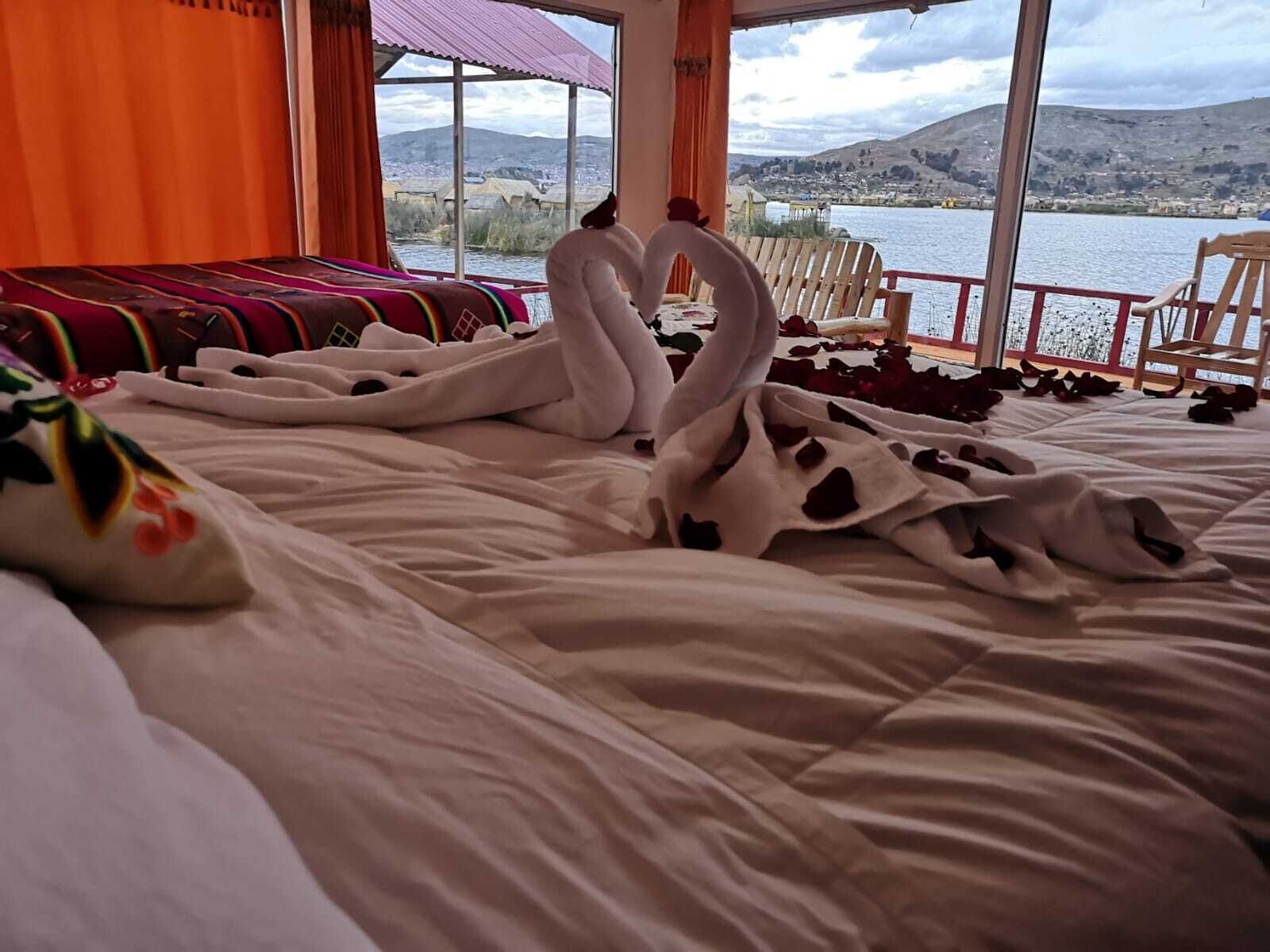 A bed with a large swan-shaped pillow arrangement and a view of a lake and mountains through large windows.