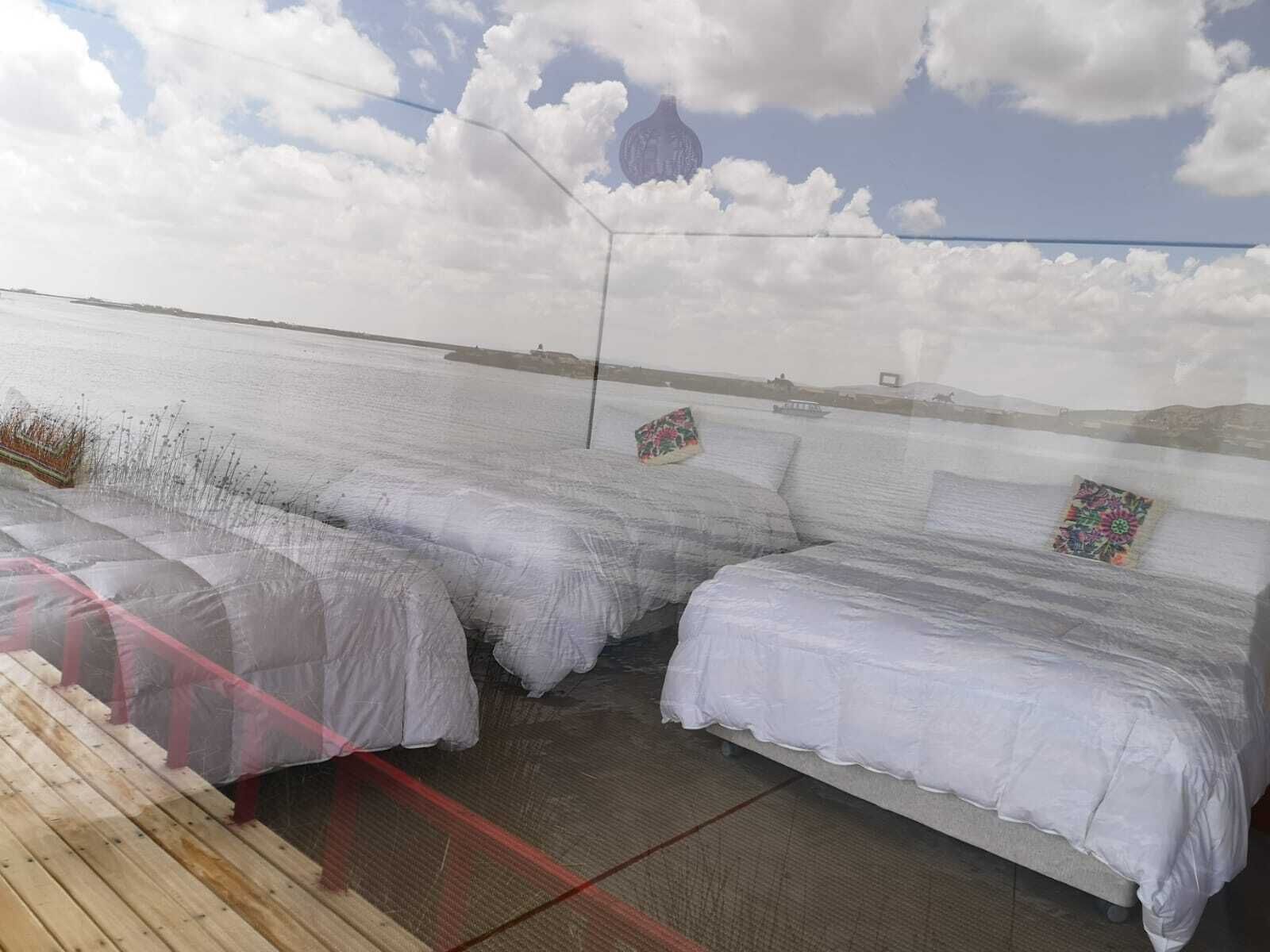 Een kamer met twee bedden voorzien van witte lakens, een houten terras en uitzicht op zee en wolken.