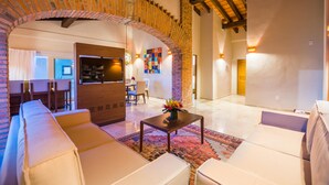Un salón espacioso con un amplio sofá, una mesa de centro con un arreglo floral y un arco de ladrillo que conduce a otra habitación.