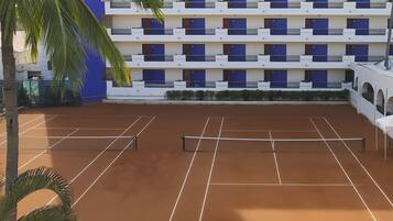 A tennis court with a net, surrounded by a building with multiple balconies and windows.