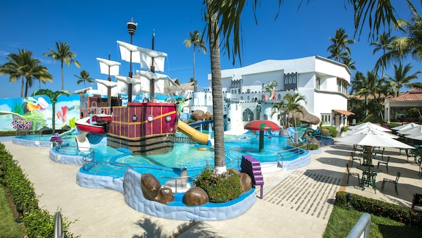 A pool area with a pirate ship, palm trees, and a castle-like building.