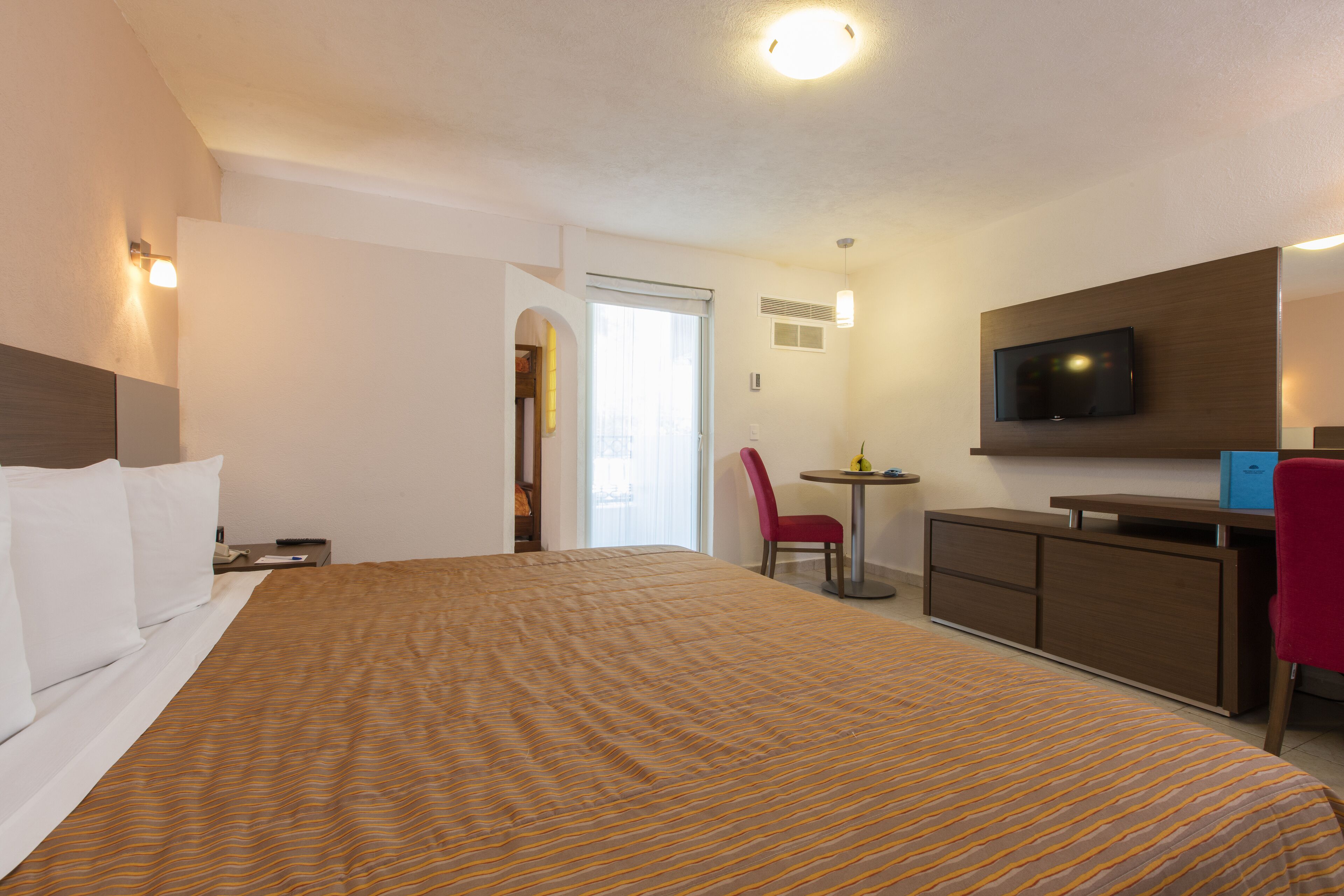 Een hotelkamer met een groot bed, een bureau, een stoel, een televisie en een deur naar een balkon.