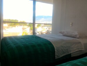 A room with a bed, a window, and a view of buildings and mountains. - Hotel CSI Medellín (Medellín)