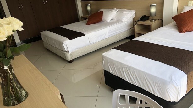 A hotel room with two beds, a wooden desk, a white chair, and a vase with flowers. - Hotel CSI Medellín (Medellín)