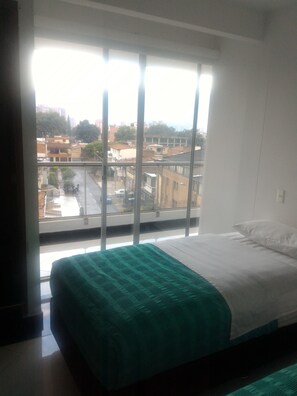 A bedroom with a large window, a bed with a green blanket, and a view of a cityscape. - Hotel CSI Medellín (Medellín)