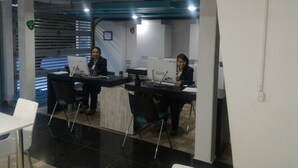An office space with two workstations, each with a computer and a chair. There is a white table in the foreground and a staircase in the background. - Hotel CSI Medellín (Medellín)
