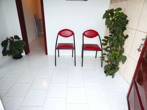 A hallway with two red chairs, a potted plant, and a tiled floor. - Apartamento Alta Vista Gramado (Gramado)