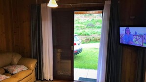 A cozy living room with a sofa, curtains, a television, and a view of a car outside. - Residencial Serra Grande Gramado (Gramado)