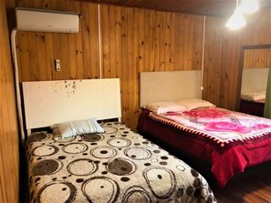 A room with two beds, wooden walls, an air conditioning unit, and a hanging light fixture.