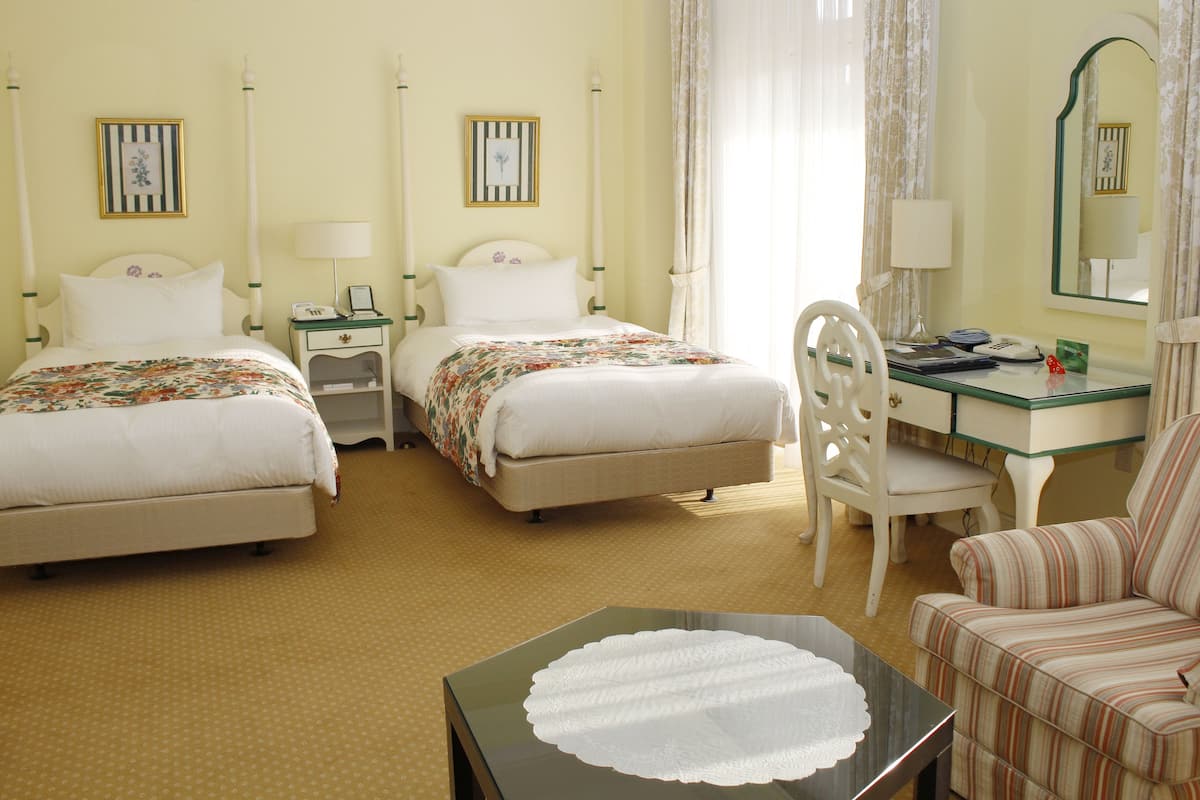A hotel room with two beds, a desk, a chair, and a small table with a placemat.
