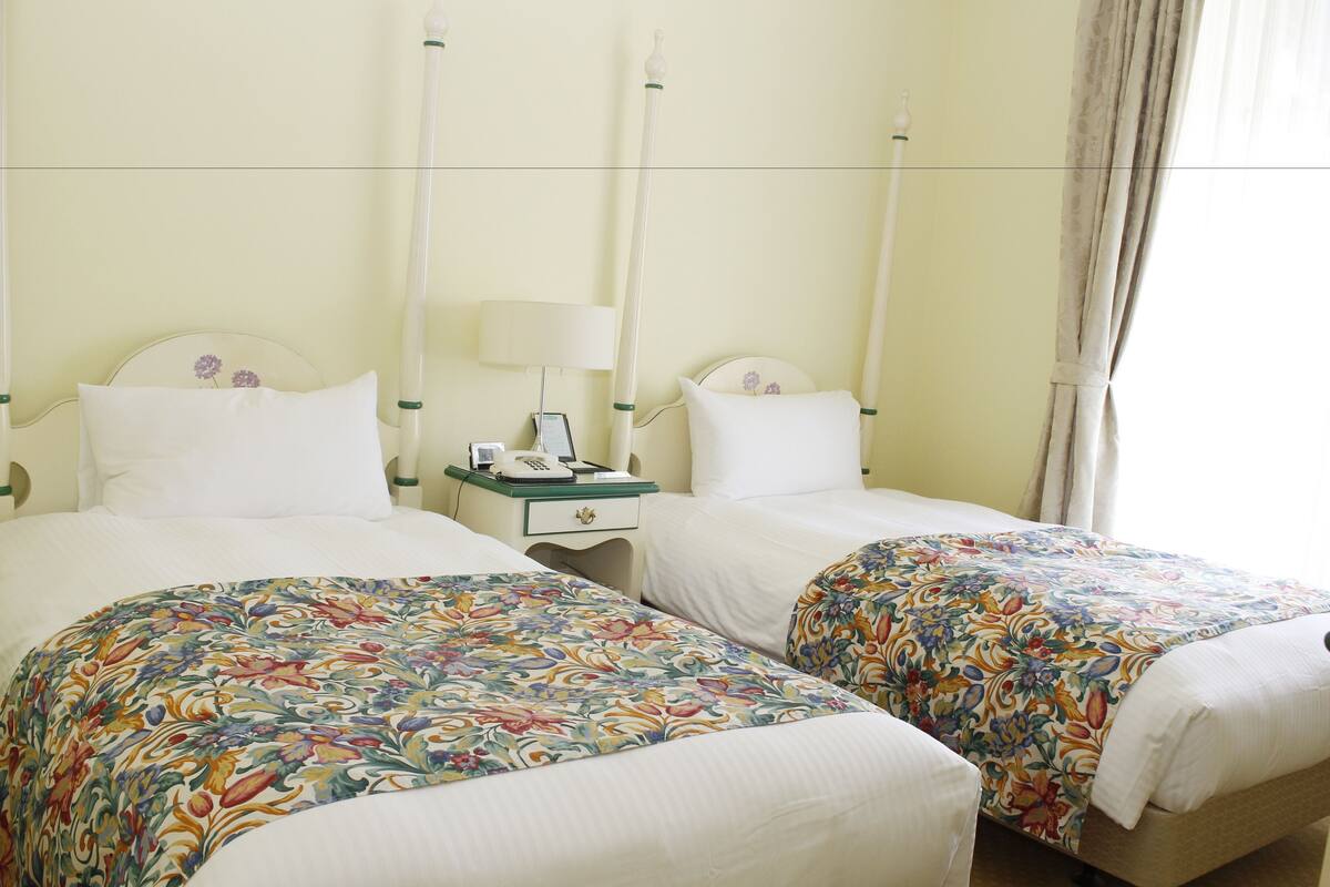 A hotel room with two beds, each with a floral bedspread, a bedside table with a lamp, and a nightstand with a telephone.