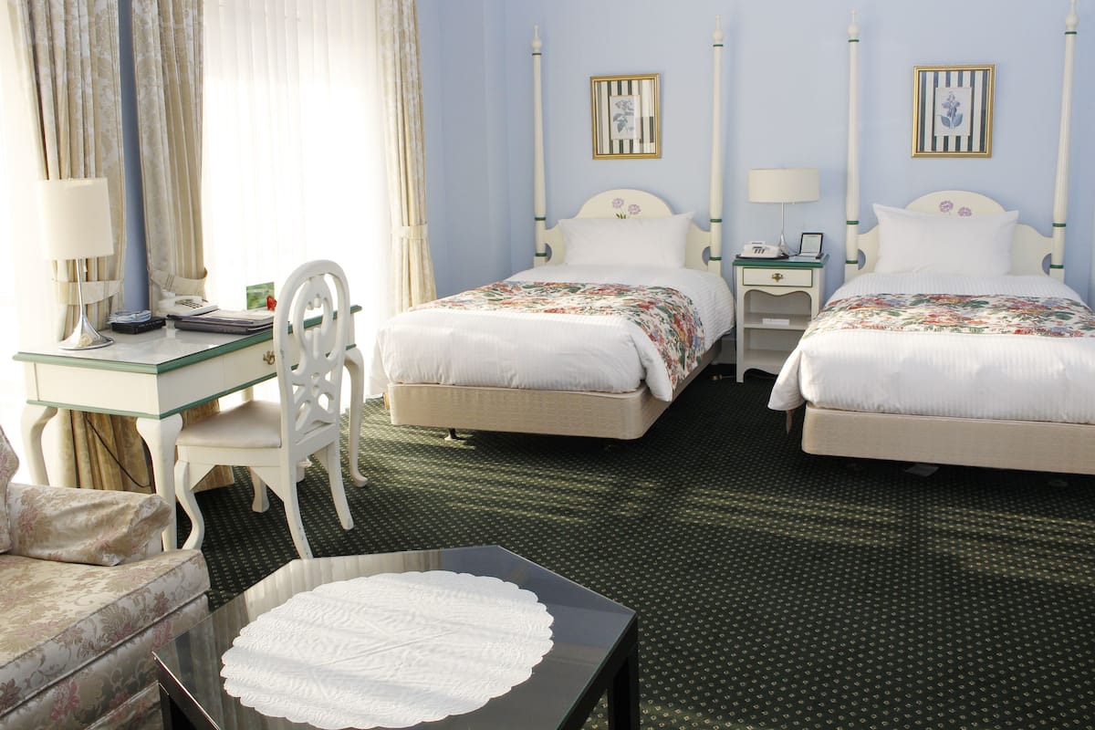 A hotel room with two beds, a desk, a chair, and a small table with a placemat.
