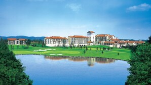 A large hotel with multiple buildings, a central tower, and a golf course with a pond in the foreground.
