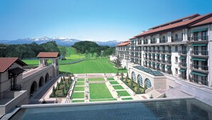 A hotel with a pool, a well-maintained lawn, and a view of snow-capped mountains.