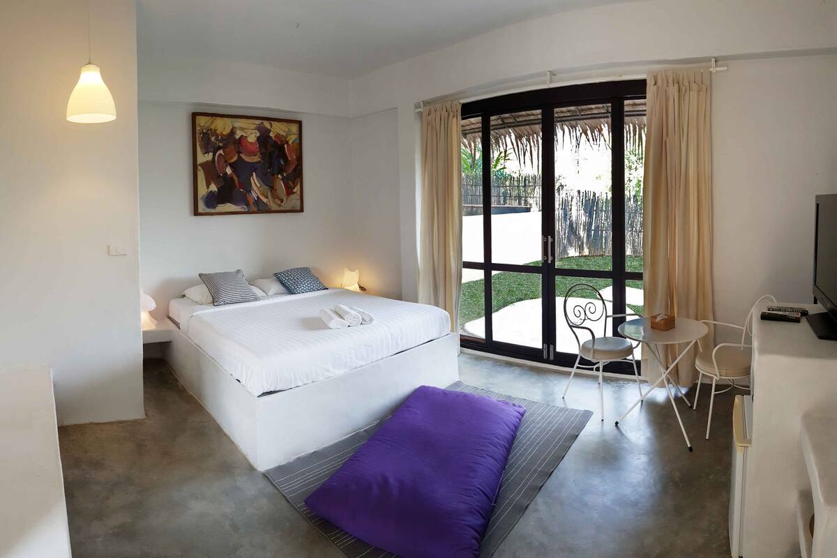 A bedroom with a bed, a painting, a window with curtains, a chair, and a TV.