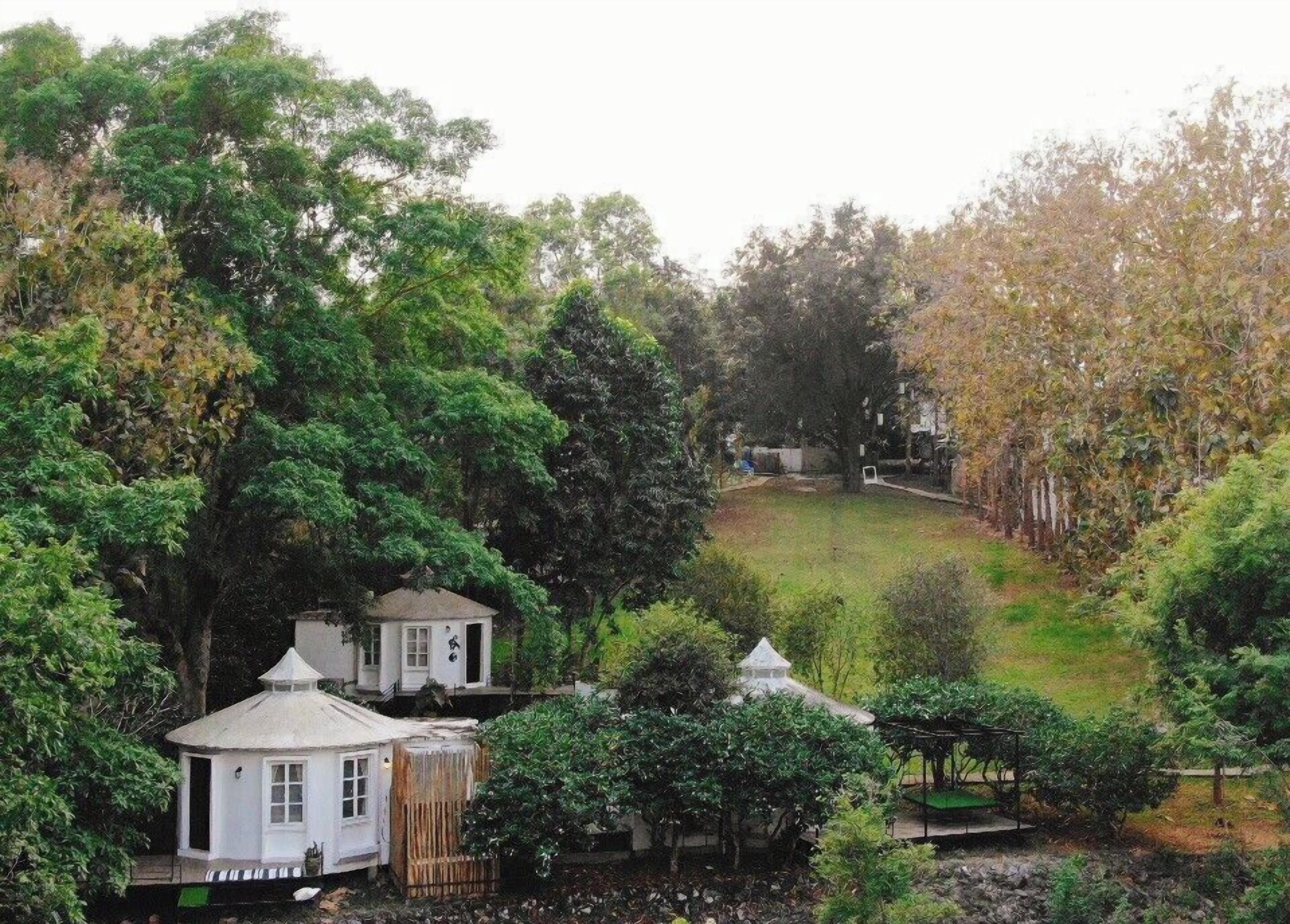 A garden with a gazebo, a small white building, and a fenced area.