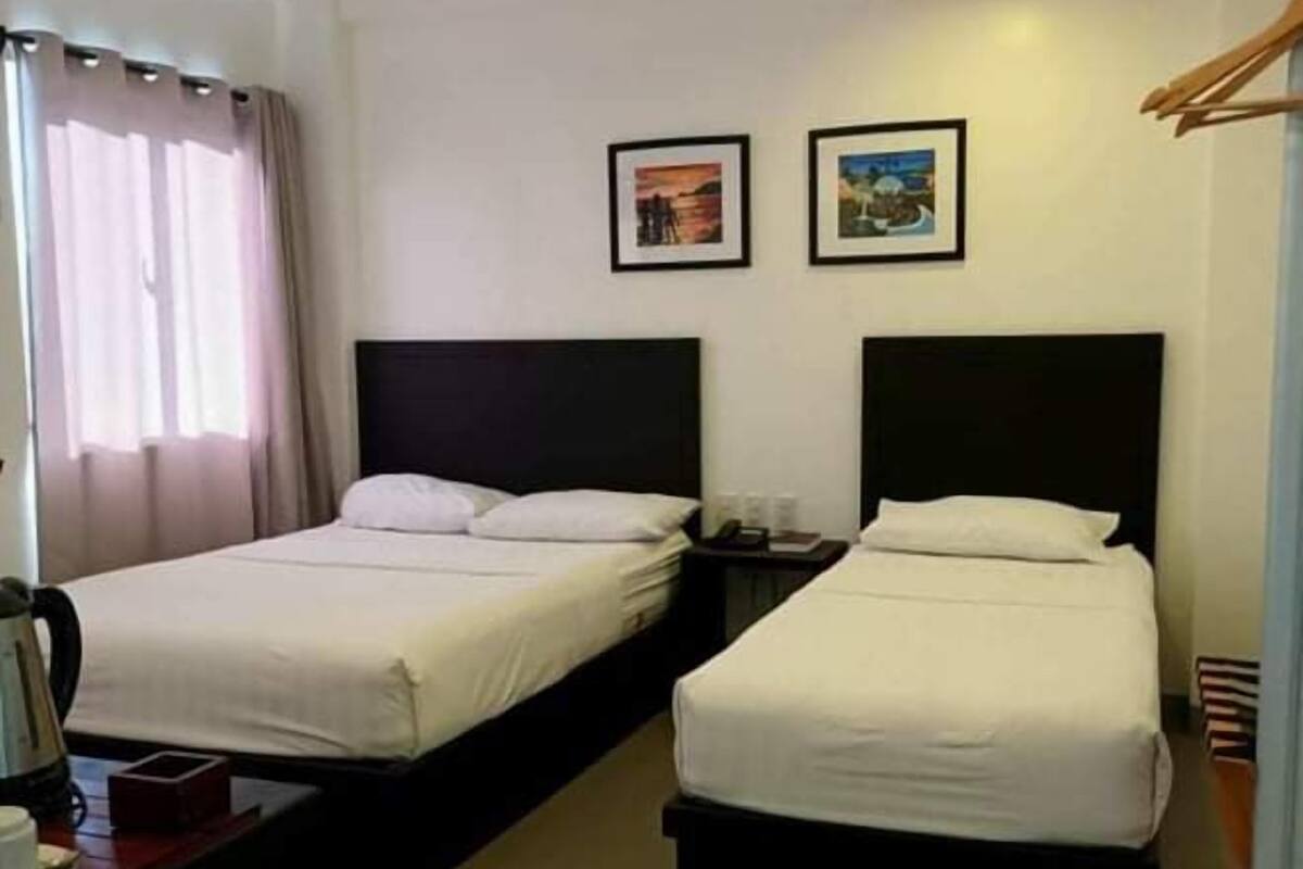 A hotel room with two beds, a nightstand, a coffee maker, and two framed pictures on the wall.