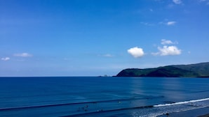 A beach with clear blue water and a distant mountain. - Playa Azul Baler (Baler)