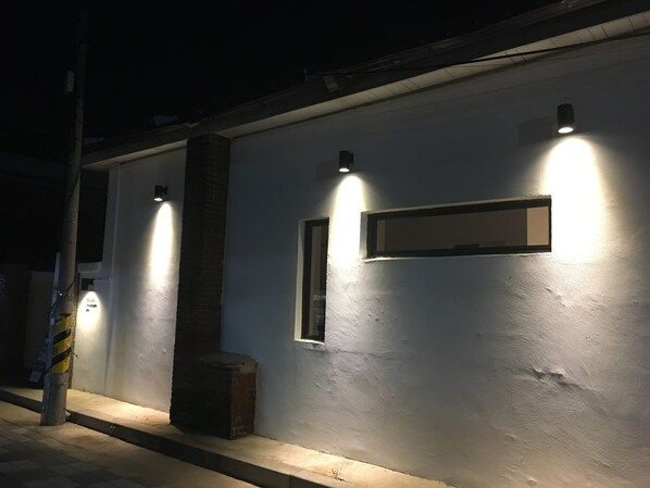 Ein Gebäude von außen bei Nacht mit beleuchteten Wandleuchten, einer Ziegelstütze und einem kleinen Fenster.