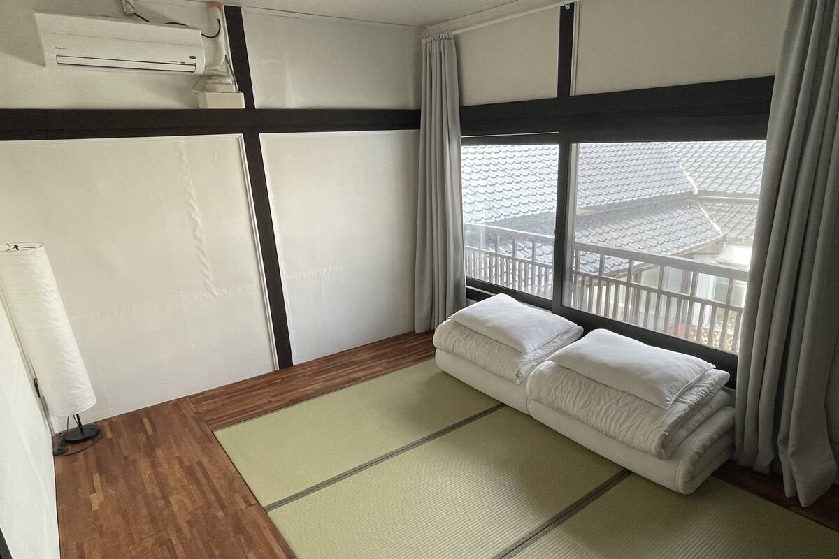 A hotel room with a tatami mat, a sofa, a window with curtains, and a view of a traditional building.