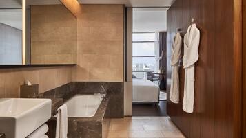 A modern bathroom with a bathtub, a large mirror, and a view of the city through a large window.