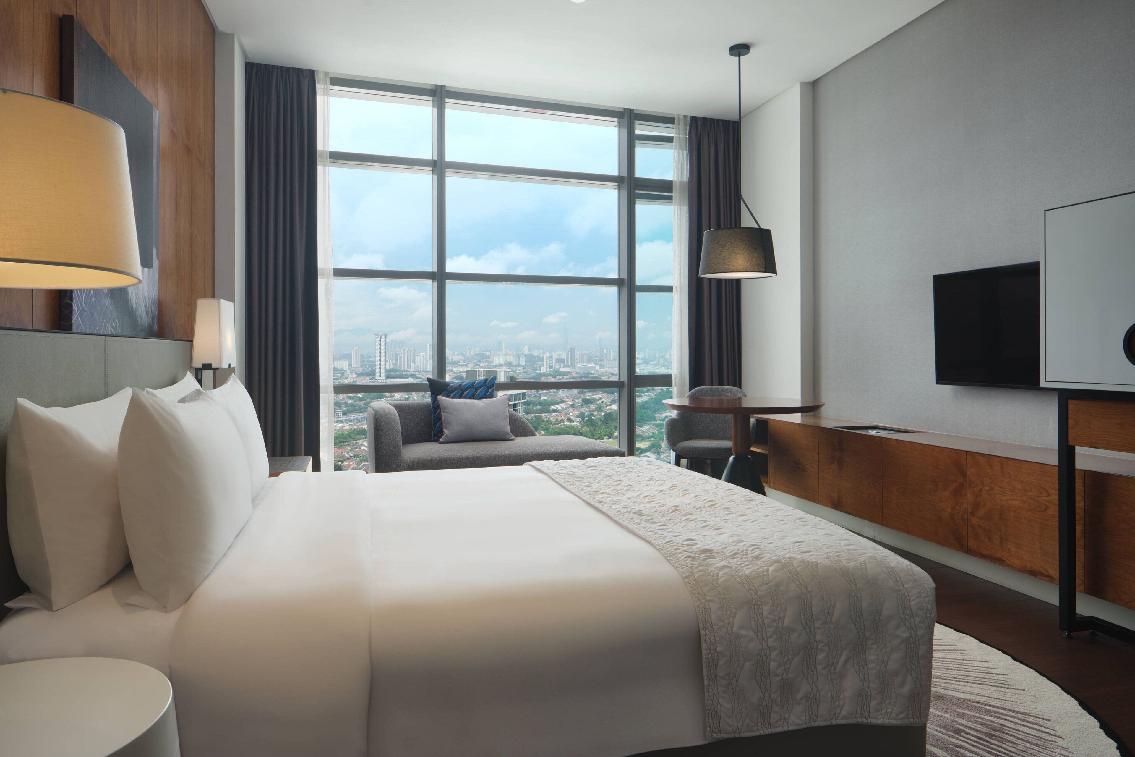 Habitación de hotel moderna con una cama grande, un escritorio, un televisor y vistas a la ciudad.
