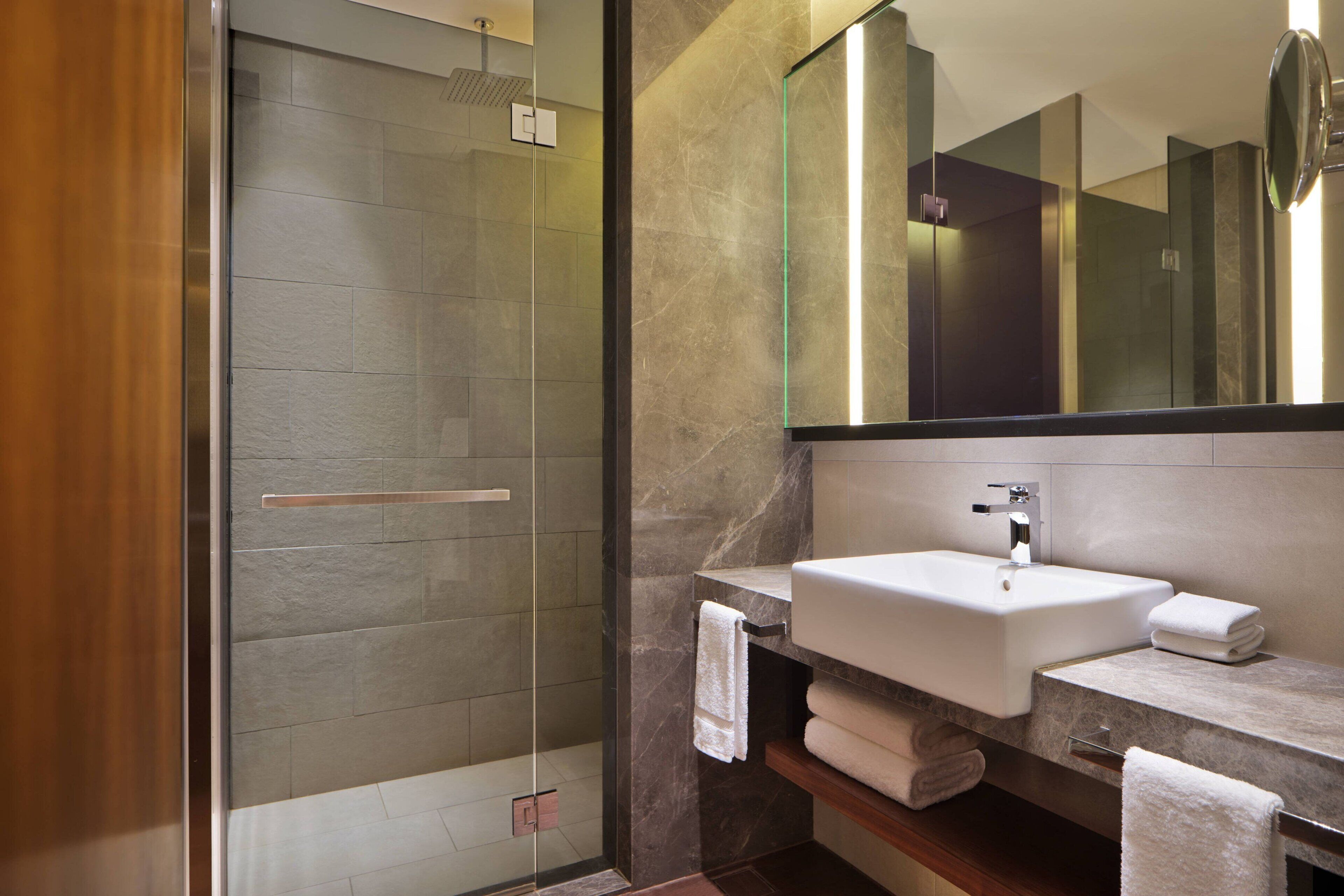 Un bagno moderno con doccia vetrata, un ampio specchio e un piano in marmo con lavabo e porta asciugamani.