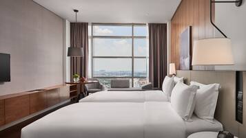 A modern hotel room with a large bed, a desk, a chair, a TV, and a view of the city.