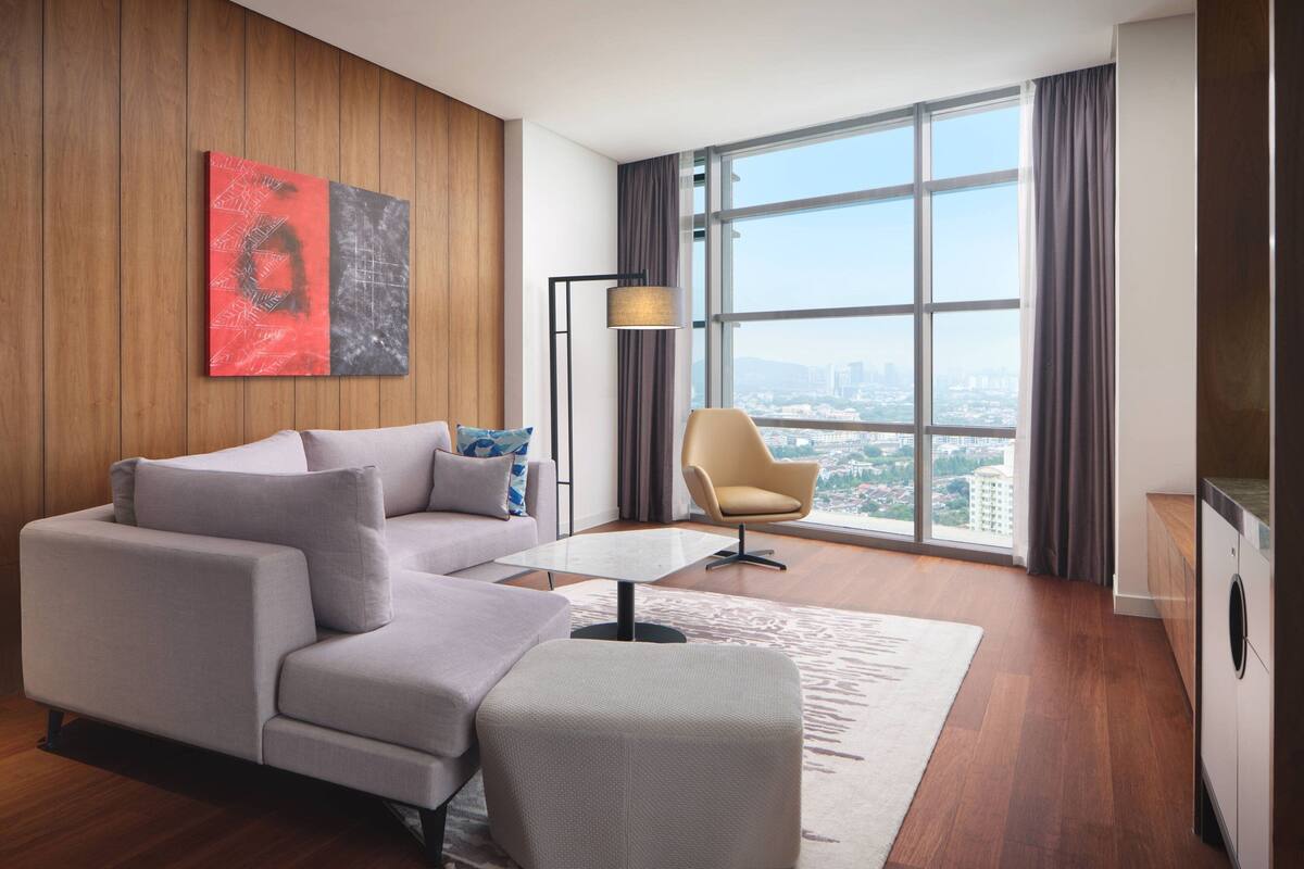 Ein modernes Wohnzimmer mit Sofa, Sessel und Couchtisch. Ein großes Fenster mit Vorhängen, eine Stehlampe und Blick auf die Stadt.