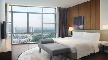 A hotel room with a large window, a bed with a grey bench, a wooden panel wall, and a painting.
