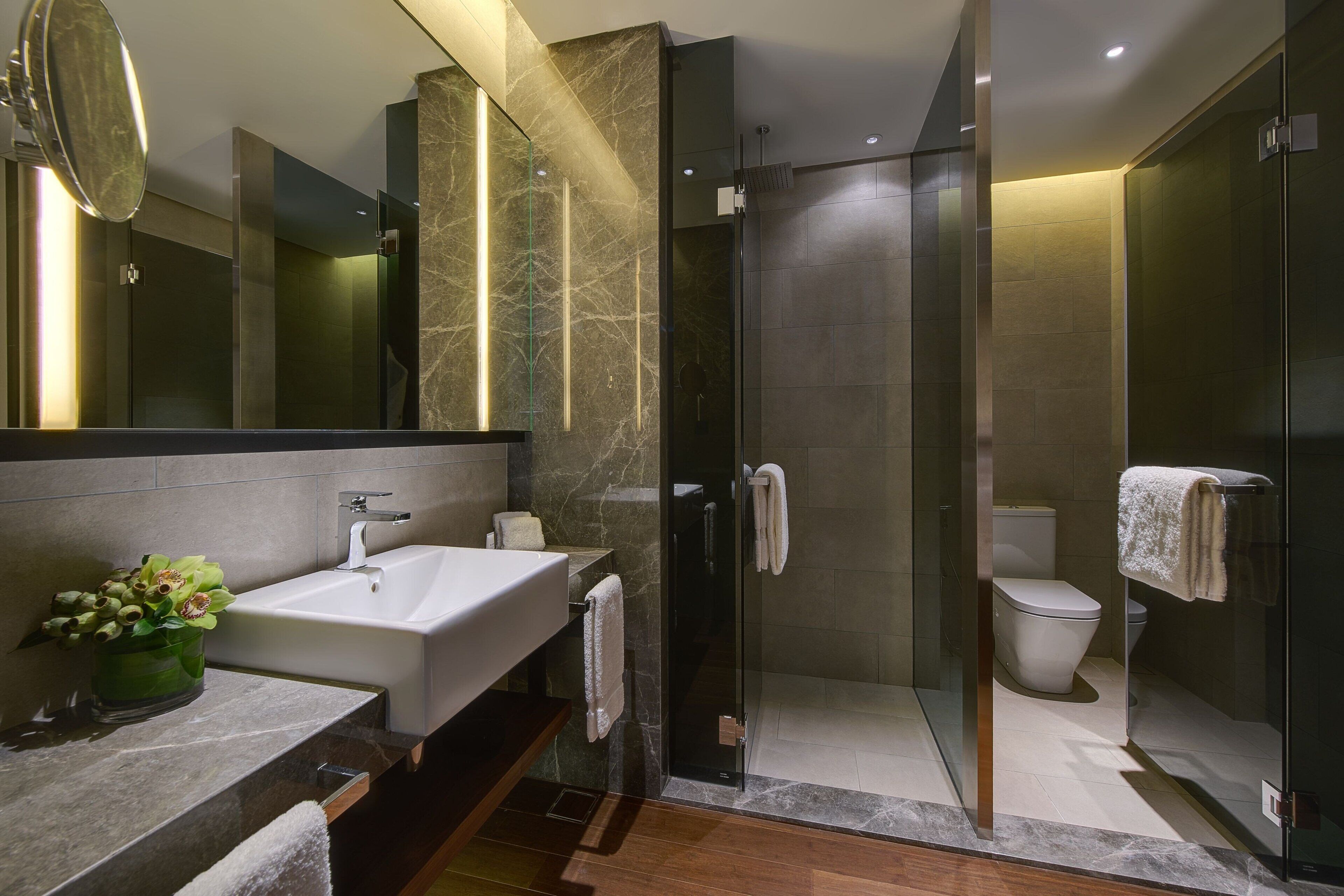 A modern bathroom with a large sink, mirror, and glass-enclosed shower.