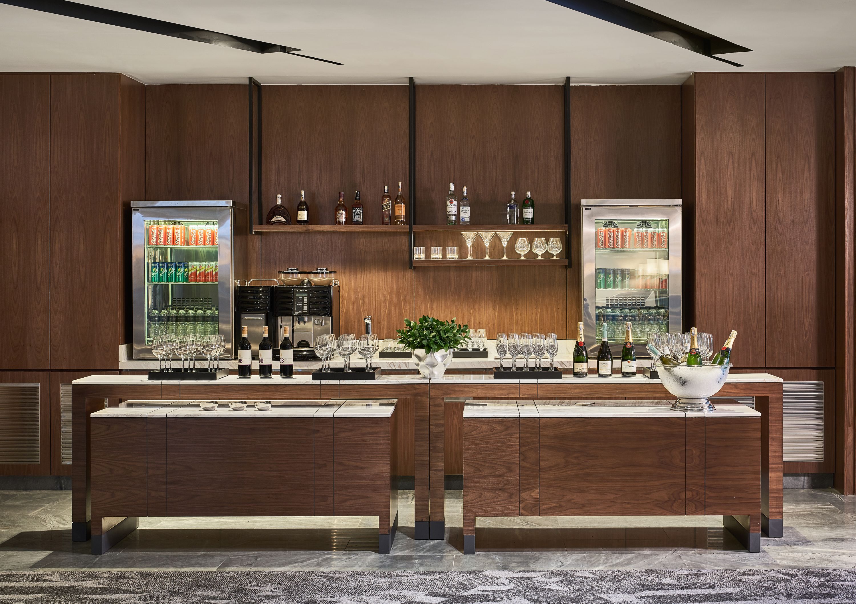 A bar area with wooden cabinets, shelves with bottles and glasses, and a marble countertop.