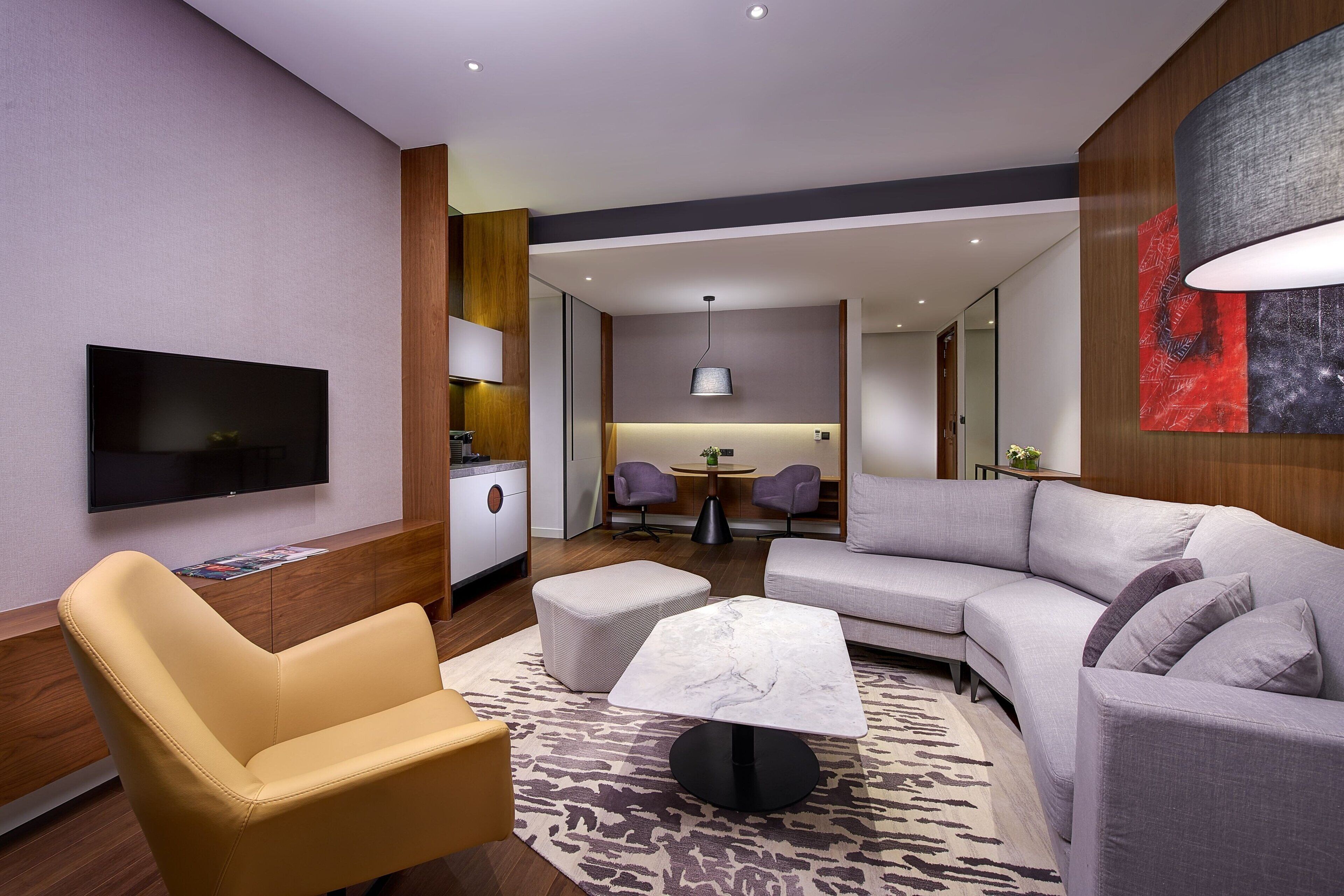 A modern living room with a flat-screen TV, a sofa, a coffee table, and a dining area in the background.