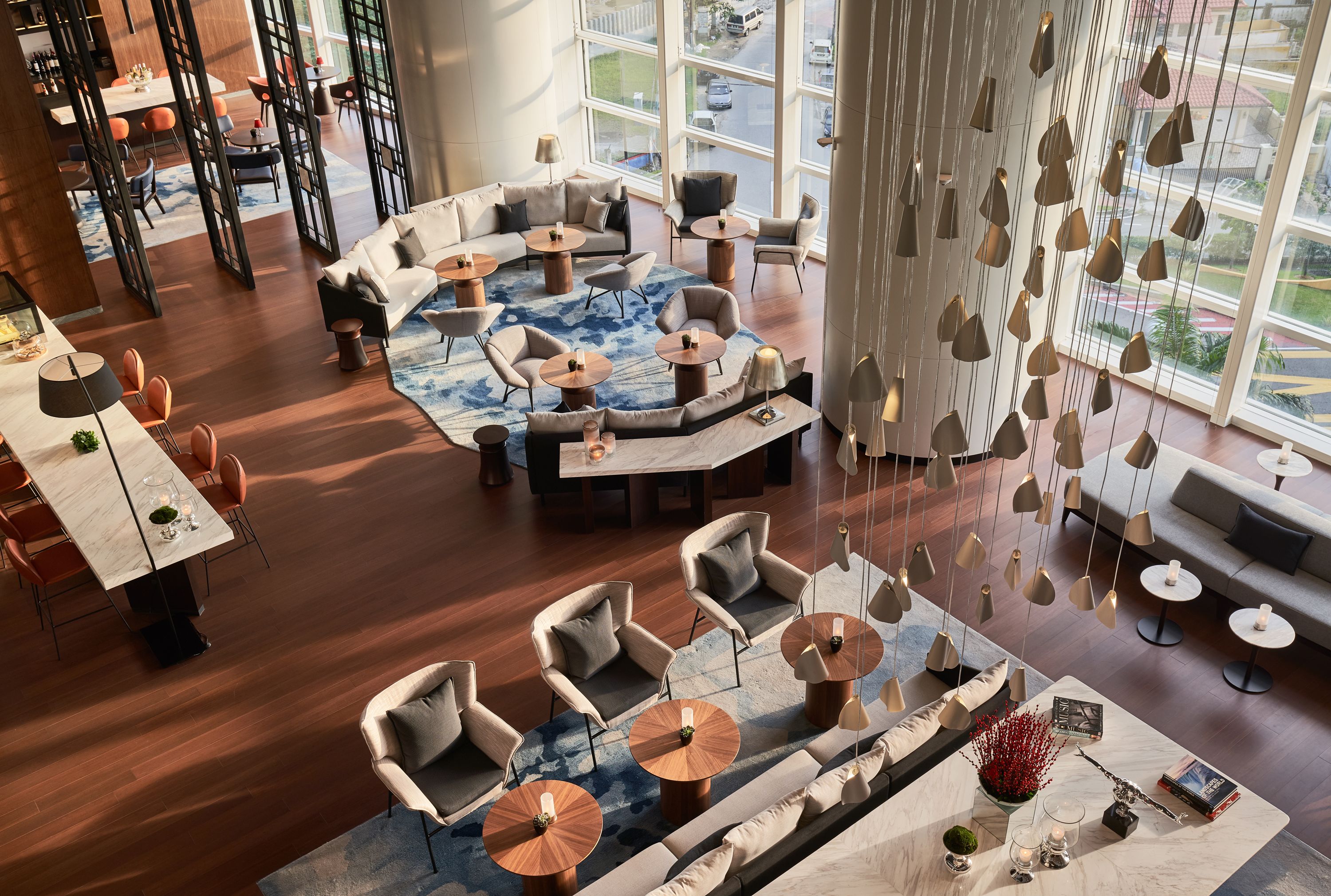 A spacious lounge area with a central seating arrangement, multiple tables, and hanging pendant lights.
