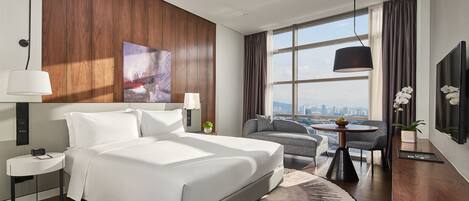A modern hotel room with a large bed, a desk, a chair, a round table, and a city view.