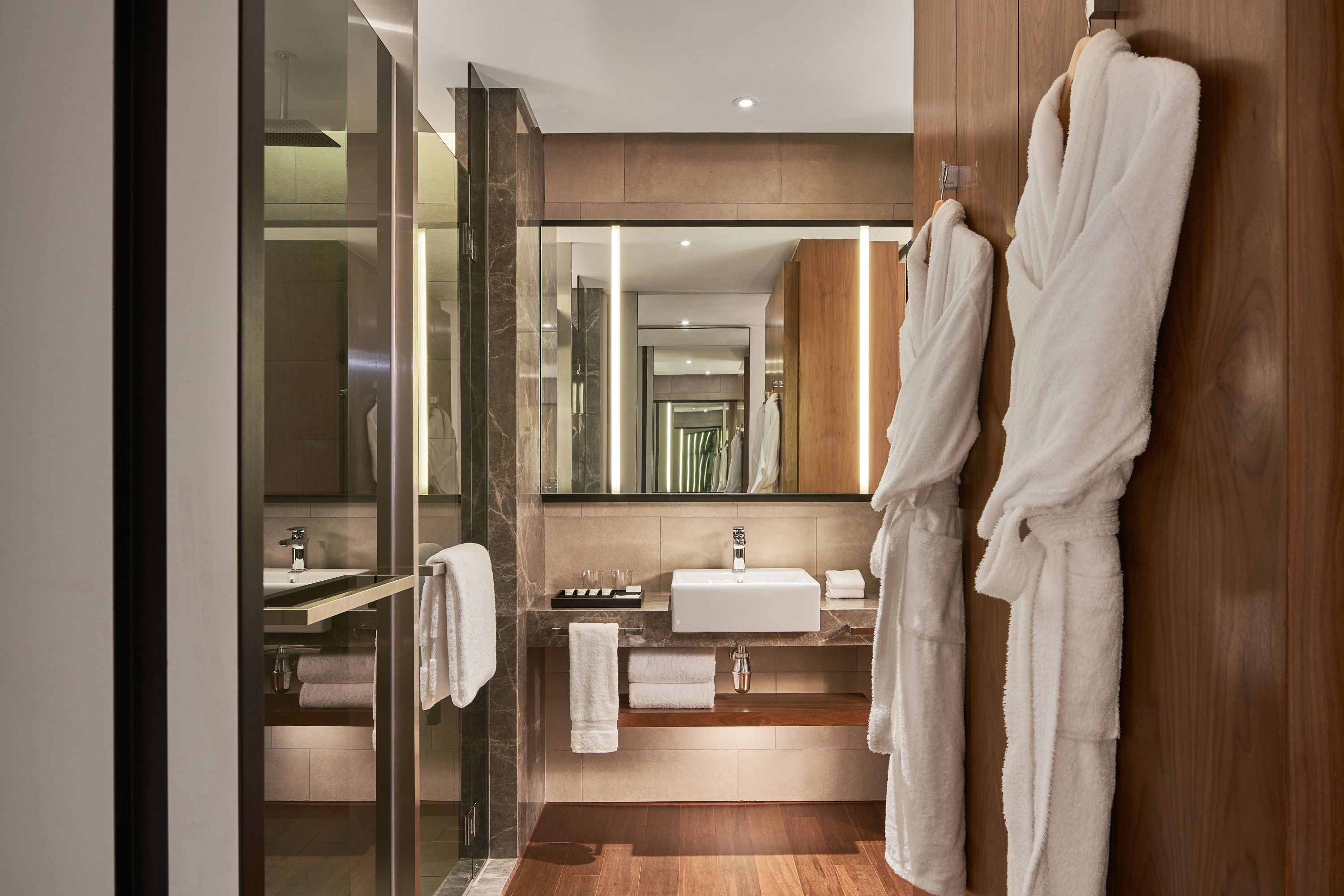 A modern bathroom with a glass shower enclosure, a wooden vanity, and two white towels hanging on the wall.