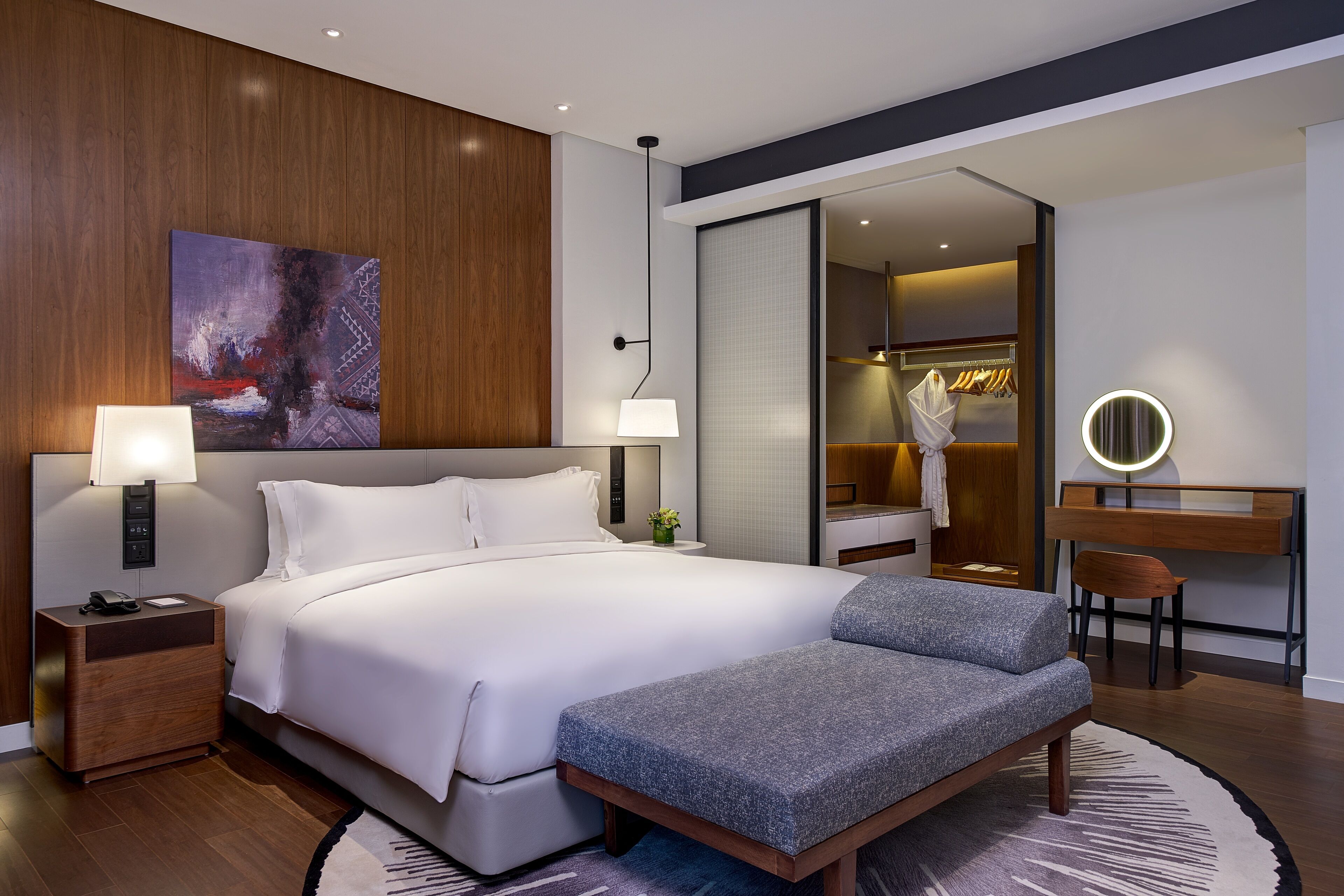 Una habitación de hotel moderna con una cama grande, lámparas de noche, un escritorio con una silla, un espejo y un vestidor.