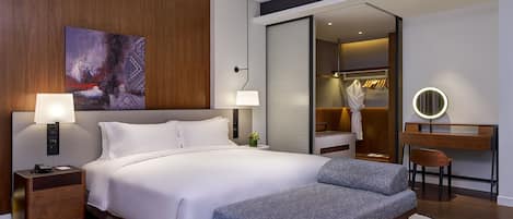 Una habitación de hotel moderna con una cama grande, lámparas de noche, un escritorio con una silla, un espejo y un vestidor.