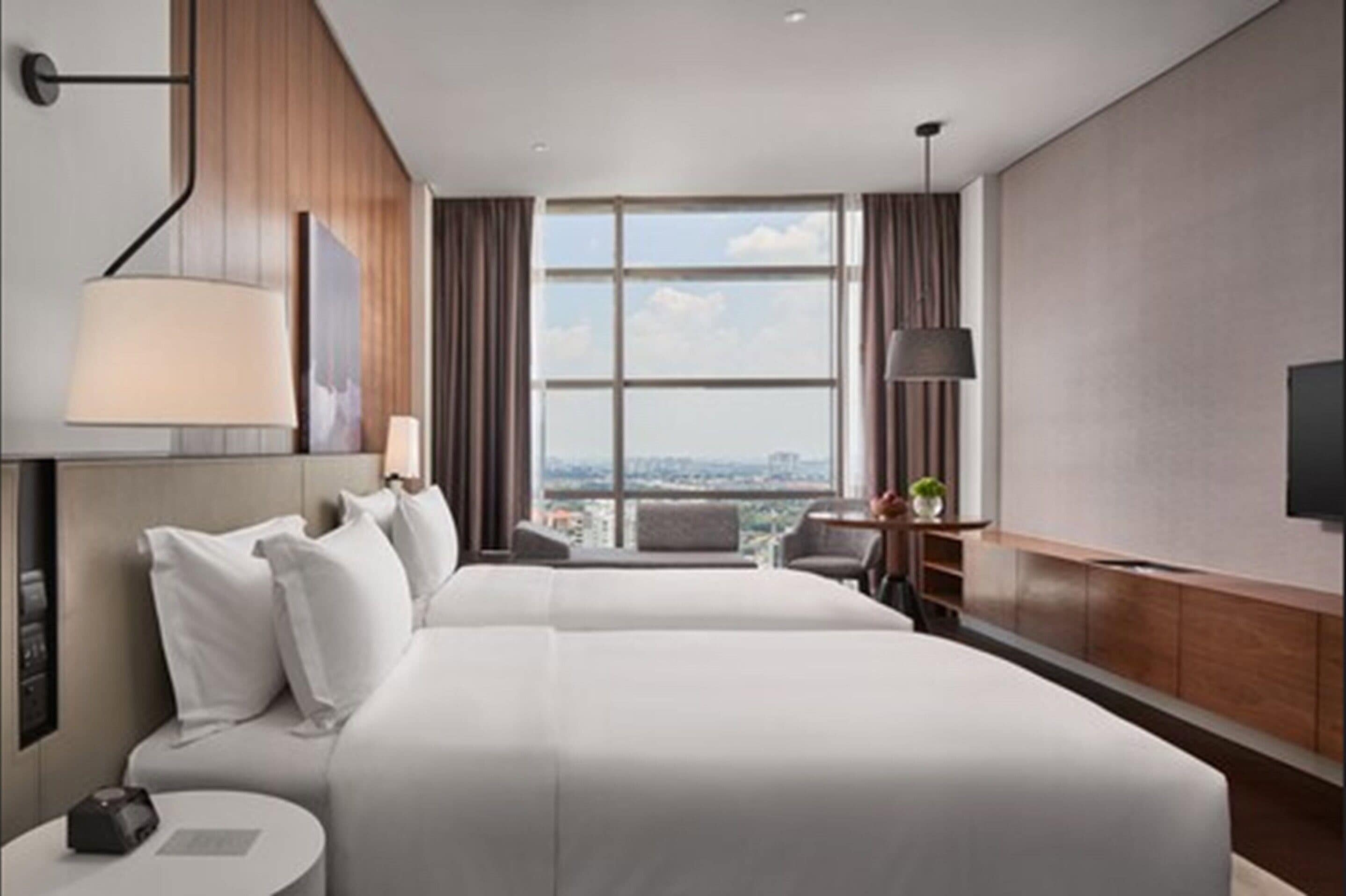Habitación de hotel con una cama grande, un escritorio, una silla, un televisor y una ventana con vista a la ciudad.